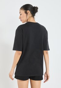 Sort bomulds T-shirt med korte ærmer og en afslappet pasform. Har en rund halsudskæring og en glat tekstur. Bæres med sorte shorts.