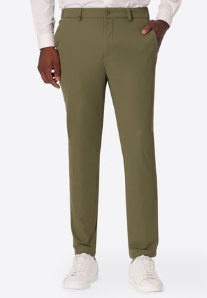Uomo che indossa pantaloni slim fit verde oliva con motivo strutturato, abbinati a sneakers bianche e camicia bianca.