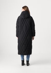 Duga crna puffer jakna s kapuljačom, s dijamantnim šavovima, zatvaranjem na patentni zatvarač i bočnim džepovima. Nosi se preko svijetloplavih traperica i čizama s petom.