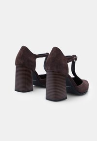 Zapatos de tacón alto de ante marrón con diseño de correa en T, que cuentan con punta cuadrada y tacones de bloque de madera texturizada.