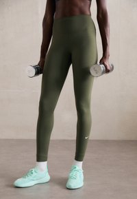 Olíva zöld leggings magas derékkal, akárcsak a menta zöld sportcipők, ezüst kézi súlyzókkal a kezében. Simaság, rugalmas anyag.
