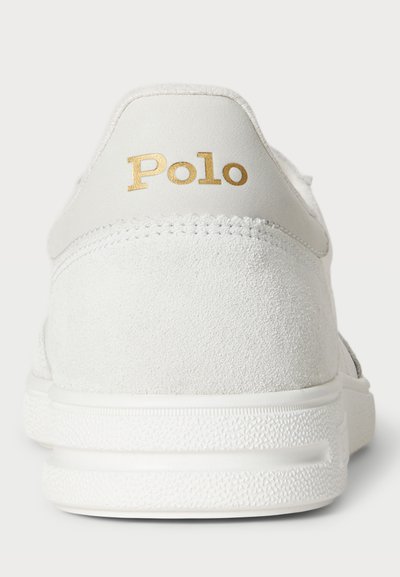 Sneaker bianco in suede con superficie texturizzata, caratterizzato da un logo dorato "Polo" sul tallone e una suola in gomma bianca per una presa ottimale.
