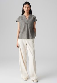 Top corto grigio con trama, maniche corte e scollatura a V, abbinato a pantaloni larghi color crema. Il top presenta una vestibilità morbida e sottili linee verticali.