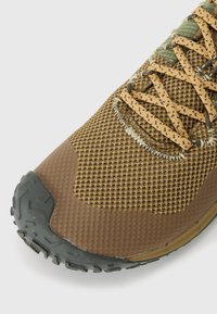 Chaussure de sport en mesh marron avec une surface texturée, des lacets à motifs et une semelle en caoutchouc noir robuste pour une meilleure adhérence. Couture détaillée le long des bords.