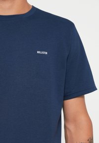 Navyblaue Baumwoll-T-Shirt mit Rundhalsausschnitt und kurzen Ärmeln, mit einem kleinen weißen "HOLLISTER"-Logo auf der linken Brustseite.