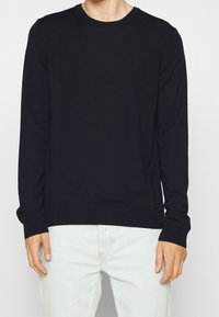 Czarny sweter dziany z długim rękawem, z okrągłym dekoltem, ściągaczami na mankietach i dole, o gładkiej fakturze, z subtelnym logo marki na dolnym boku.