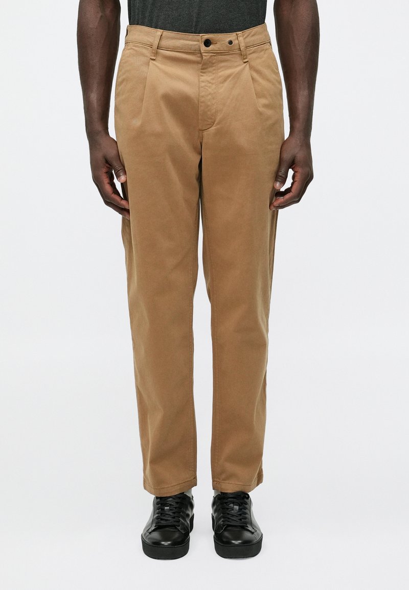 Tan chinos with a relaxed fit, featuring a flat front, side pockets, and a smooth cotton texture, paired with black sneakers.