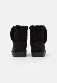 Bottines en suede noir avec une douce doublure en fausse fourrure, un haut arrondi et une semelle en caoutchouc plate, présentant des coutures le long des coutures arrière.