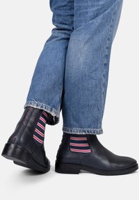 Czarne skórzane buty chelsea z elastycznymi bocznymi panelami, w połączeniu z niebieskimi dżinsami i paskowymi skarpetami w czerwono-białe paski. Gładkie wykończenie.