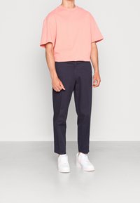 Kurze Ärmel, verkürztes, rotes Baumwoll-T-Shirt, kombiniert mit dunkelblauen Hosen und weißen Sneakers mit rosa Akzenten. Einfaches, klares Design.
