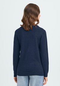 Mörkblå tröja i mjukt material med långa ärmar, rund halsringning och ribbad nederkant. Enkel och minimalistisk design.
