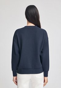 Felpa blu navy realizzata in tessuto morbido, con collo rotondo, spalle scese e polsini a costine. Design semplice e minimalista.