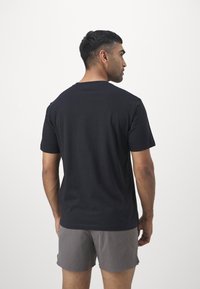 Schwarzes kurzärmeliges T-Shirt aus Baumwolle mit rundem Ausschnitt, von hinten gesehen, kombiniert mit grauen Shorts. Glatte Textur, keine sichtbaren Muster.