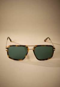 Tortoiseshell sunglasses with dark green lenses, angular frame design, metal accents, and thin temples showcasing a modern aesthetic.