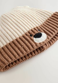 Knitted hat with a cream top and a brown ribbed band. Features a bear face with embroidered eyes and a snout in the brown section.