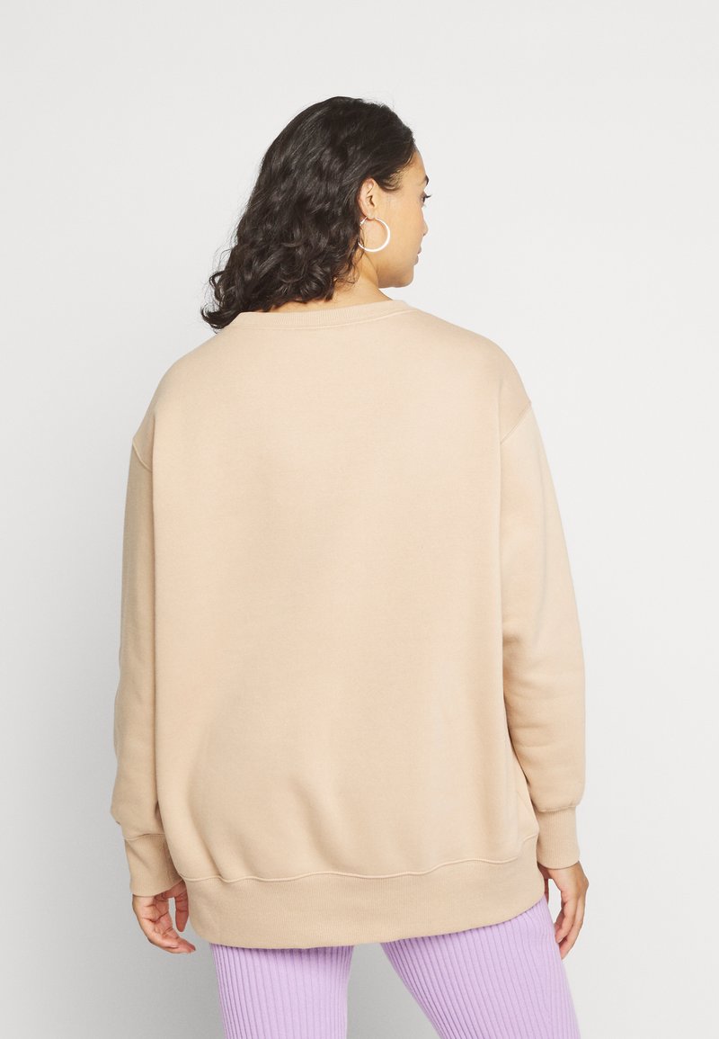 Sweatshirt surdimensionné couleur crème avec des poignets et un ourlet à côtes, présentant un design simple et une texture douce, porté avec un pantalon lilas à côtes.