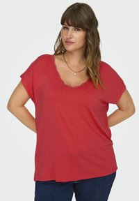 Červené tričko s krátkým rukávem a kulatým výstřihem, s krajkovým lemem kolem výstřihu. Měkká tkanina s uvolněným střihem.