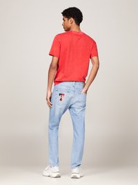 Rød t-skjorte med kort arm og rund hals, sammen med lyseblå denimjeans med et logo-merke på baklommen og hvite sneakers.
