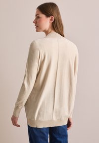 Crème-kleurige lange mouw trui met een relaxte pasvorm, geribde manchetten en zoom. Bevat een zachte textuur en een centraal naaddetail op de rug.