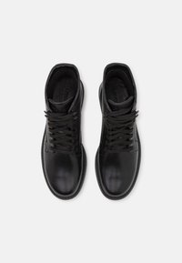Botas de cuero negras hasta el tobillo con punta redonda, cordones y un ribete cosido. Textura suave con un collar acolchado para mayor comodidad.