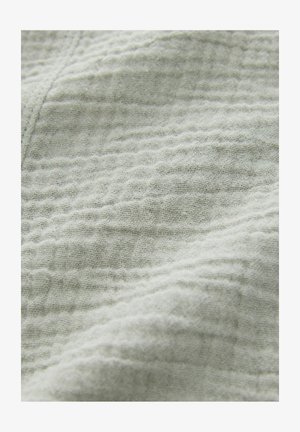 Textúrovaná svetlošedá tkanina s waflovým vzorom, obsahujúca jemné, mäkké vlákna a drobné variácie v tkaní pre zvýraznenie hĺbky.