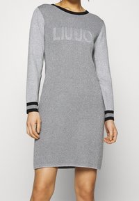 Graues Strickkleid mit langen Ärmeln, schwarzem geripptem Ausschnitt und kontrastierenden schwarz-grauen gestreiften Bündchen mit strukturiertem Finish.