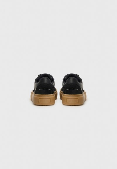 Svarta sneakers med en strukturerad ovandel, med en vadderad krage och en kraftig brun gummisåle. Minimal sömnadsdetaljer.