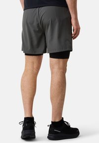 Grijze sportshorts met een gladde textuur, knielange snit en eronder zwarte compressieshorts. Draagt dit met zwarte sportschoenen.