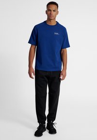 Blå t-shirt med rund hals i mjukt tyg, kortärmad, matchad med svarta träningsoverallsbyxor, svarta snörskor, minimal logotypdetalj.