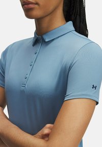 Svetlomodrá polo košela vyrobená z hladkého, elastického materiálu. Obsahuje golier, zapínanie na gombíky a logo na ľavom rukáve. Krátke rukávy.