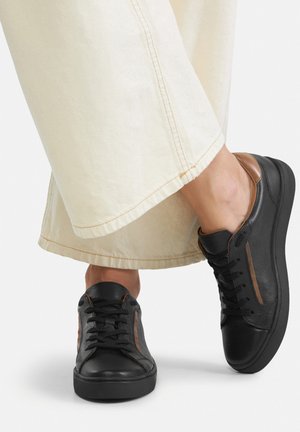 Sneakers in pelle nera con dettagli marroni; design a taglio basso, chiusura con lacci, superficie testurizzata e suola in gomma. Indossate con pantaloni di colore chiaro.