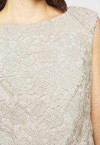 Lace-top i mjuk beige med blommönster, invecklad pärlbroderi, bred halsringning och delikat, texturerad tyg.