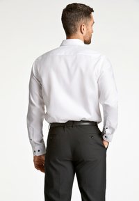 Witte langemouwen shirt met een gladde textuur, voorzien van zwarte knoopaccenten op de manchetten; gecombineerd met donkere broeken en een smalle zwarte riem.