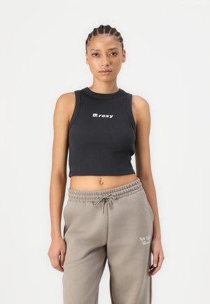 Fekete bordás crop top kerek nyakkivágással és fehér "Roxy" logóval; világosszürke melegítőnadrággal párosítva, amely gumis derékkal és logóval rendelkezik.
