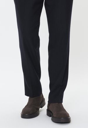 Brune ruskindsankelstøvler med en tyk sort sål, parret med mørke strukturerede bukser, der har lige snit og slim fit.