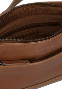 Interno della borsa in pelle marrone con una tasca con zip e un'etichetta impressa che riporta "GREEN BURRY." Texture liscia e linee pulite.