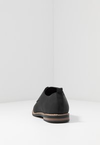 Chaussure en cuir noir avec une finition lisse, une forme arrondie et un petit talon avec des accents beiges. Comprend une languette à l'arrière.