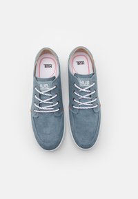 Blaue Canvas-Sneaker mit weißen Schnürsenkeln, Gummisohlen und einem auffälligen "HUB"-Logo auf der Zunge. Mit orangefarbenen Akzenten um die Ösen.