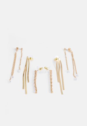 Sada náušníc v zlatej farbe so vzormi reťazí a stúh. Niektoré s priehľadnými akcentmi, rôzne dĺžky a odlišné tvary pre vizuálny záujem.