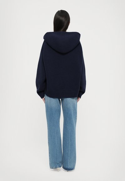 Navy blue hooded oversized sweatshirt with ribbed cuffs and hem, paired with light blue flared denim jeans. Plain textured fabric.
