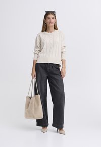 Bež pulover z vzorcem v obliki pletenega kabla, sproščen kroj, kombiniran s širokimi hlačami iz temno modrega jeansa. Drži svetlo bež torbo, obuta v koničaste gole čevlje z visokimi petami.