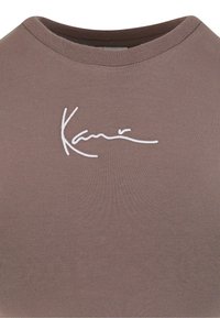 Brązowy dopasowany top na ramiączkach z prążkowanym materiałem, z białym haftowanym logo marki na klatce piersiowej i klasycznym okrągłym dekoltem.