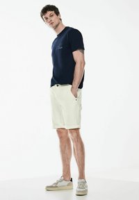 Camiseta de manga corta en color navy con logo, pantalones cortos de cargo claros y zapatillas de materiales mixtos. Tejido suave, corte relajado, dobladillos enrollados en los pantalones cortos.