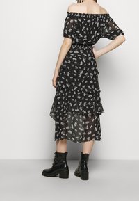 Schwarzes Off-Shoulder-Kleid mit weißem Blumenmuster, gestuften Rüschen und einem durchsichtigen Overlay. Getragen mit schwarzen Knöchelstiefeln.