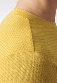 Tejido amarillo texturizado con patrones diagonales, que presenta un diseño de hombro estructurado y transiciones sin costuras entre secciones.