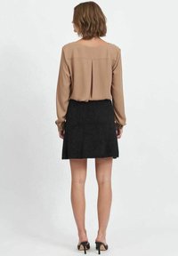 Blusa marrone a maniche lunghe con piega sul retro abbinata a una mini gonna nera testurizzata. L'outfit è completato da scarpe nere con tacco alto.