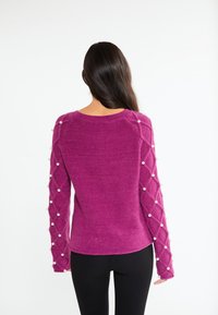 Fuchsia sweater med struktureret krop og lange ærmer prydet med et diamantmønster og hvide perleaccentuer. Glat stoffinish.