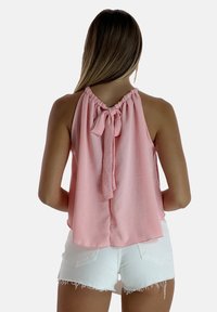 Top sin mangas rosa con escote fruncido y detalle de lazo en la parte posterior, combinado con pantalones cortos blancos deshilachados. Textura suave, ajuste casual.