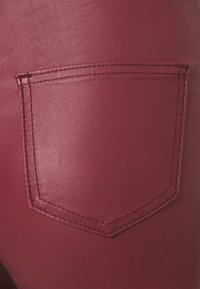 Burgundy konstläderbyxor har en solid textur med en rombformad bakficka och kontrasterande sömmar.
