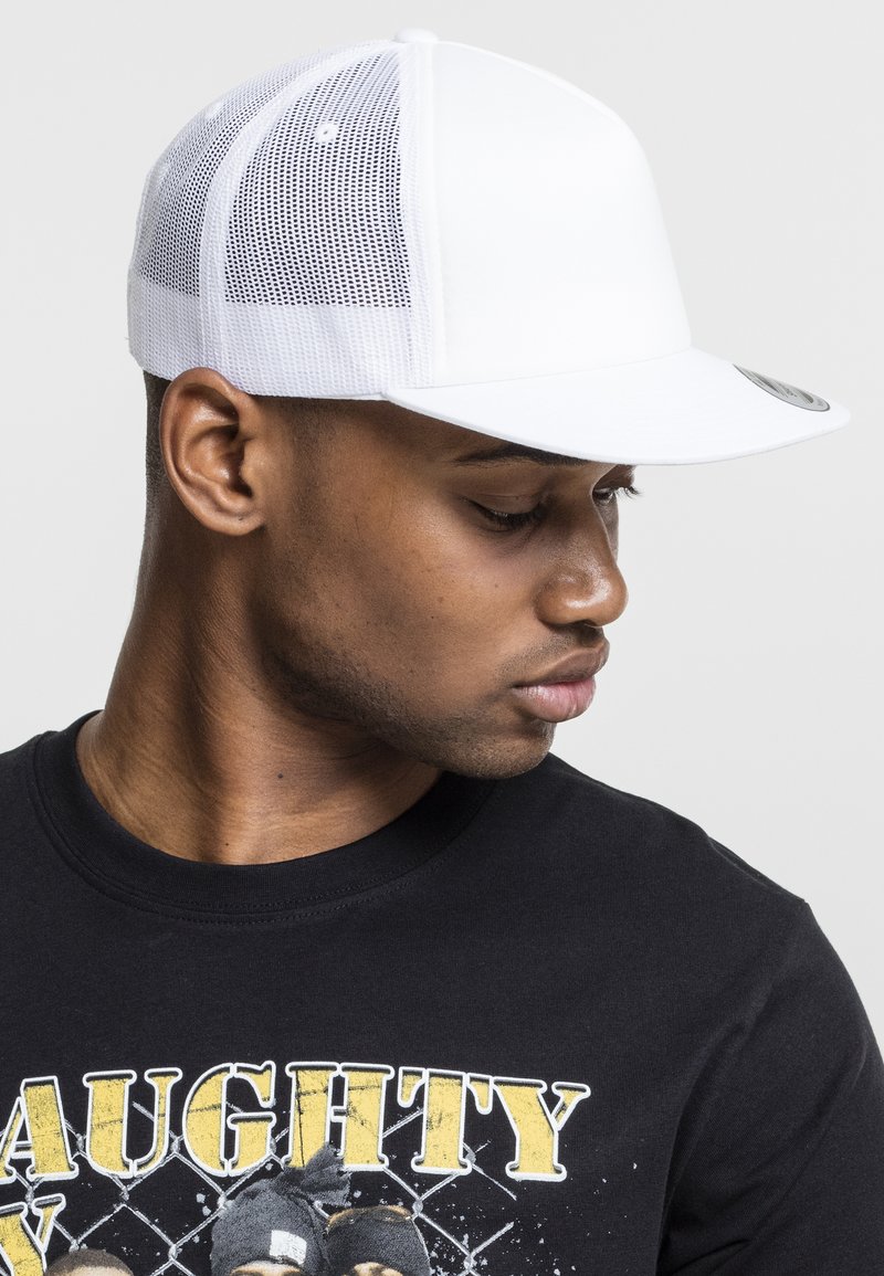 Căciulă de baseball albă cu față solidă și spate din plasă, având o vizor plat și un detaliu cu un logo circular pe vârf. Tricou grafic negru vizibil.